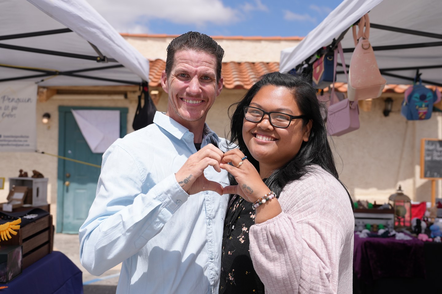 Two Kismet Community founders making a heart shape with their hands at their outdoor market booth